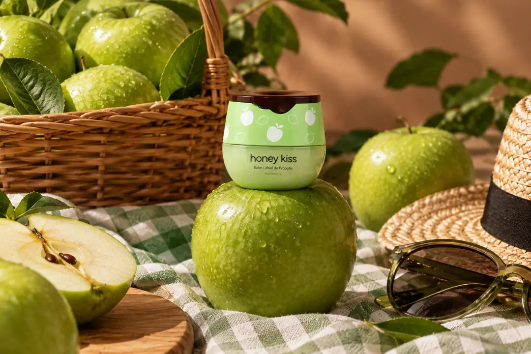 Pote do balm labial HoneyKiss sabor Maçã Verde, sobre mesa com maçãs